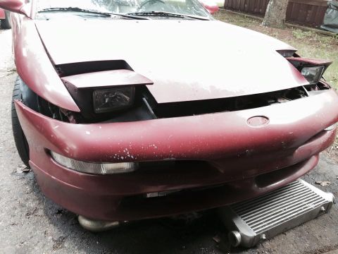 1995 Ford Probe - Front view of a red 1995 Ford Probe with its hood open, revealing a pop-up headlight assembly and a large intercooler positioned beneath th…