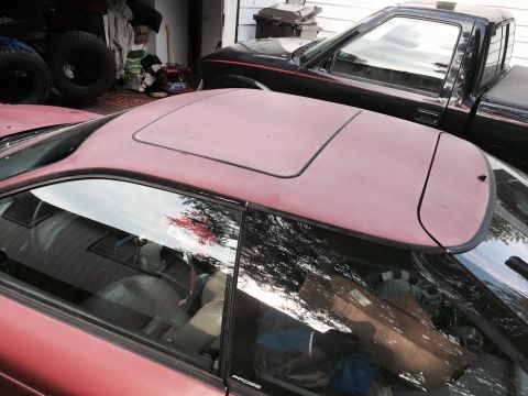 1995 Ford Probe - A close-up, high-angle view of the roof and passenger side window of a red coupe, possibly a 1995 Ford Probe, parked in a garage next to a…