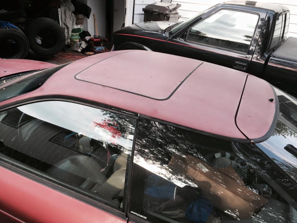 Red coupe with sunroof parked in a garage next to a black pickup truck.
