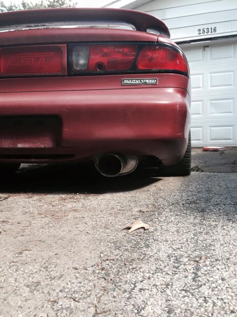 1995 Ford Probe - The rear of a red MazdaSpeed GT is shown parked in front of a white garage door with the house number 25316 visible. A chrome exhaust pipe…
