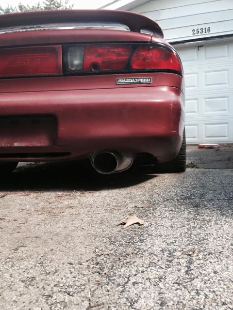 1995 Ford Probe - The rear of a red MazdaSpeed branded car is shown parked in front of a white garage door with the number 25316 visible. The car features a…