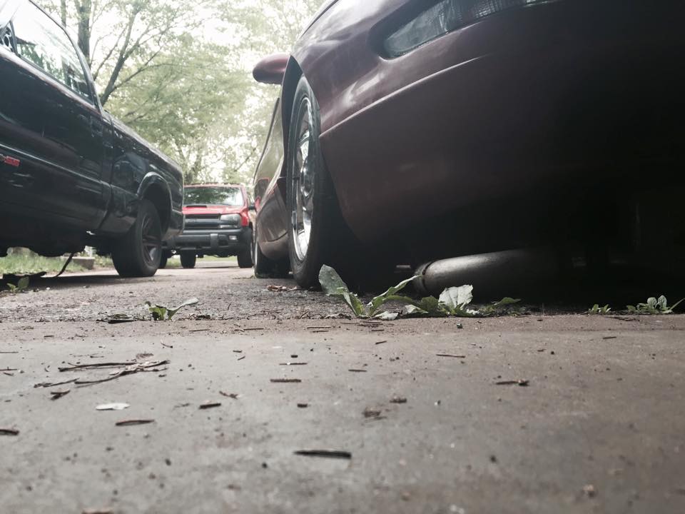 Low angle view of a red car's rear tire and exhaust, with other vehicles in the background.