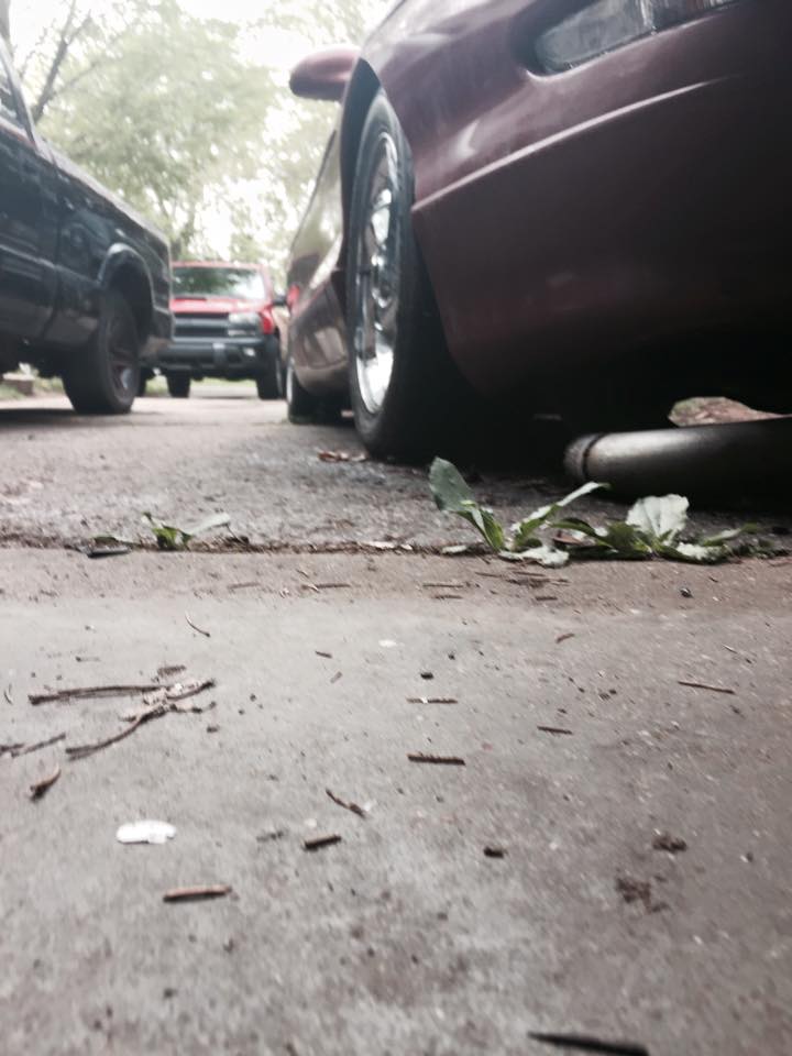 Maroon Ford Probe side view, showing rear wheel and exhaust pipe. Black pickup and red SUV in background.