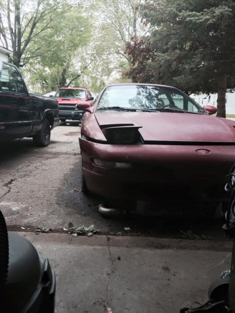 1995 Ford Probe - A maroon 1995 Ford Probe is parked in a driveway next to a black pickup truck. The Probe's hood is open, and its front end is visible.