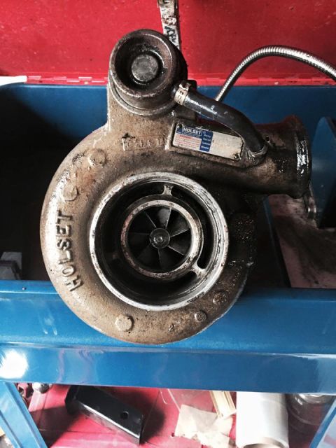 1995 Ford Probe - A turbocharger with a "HOLSET" label is mounted on a blue shelf. The turbocharger is dirty and appears to be made of metal.
