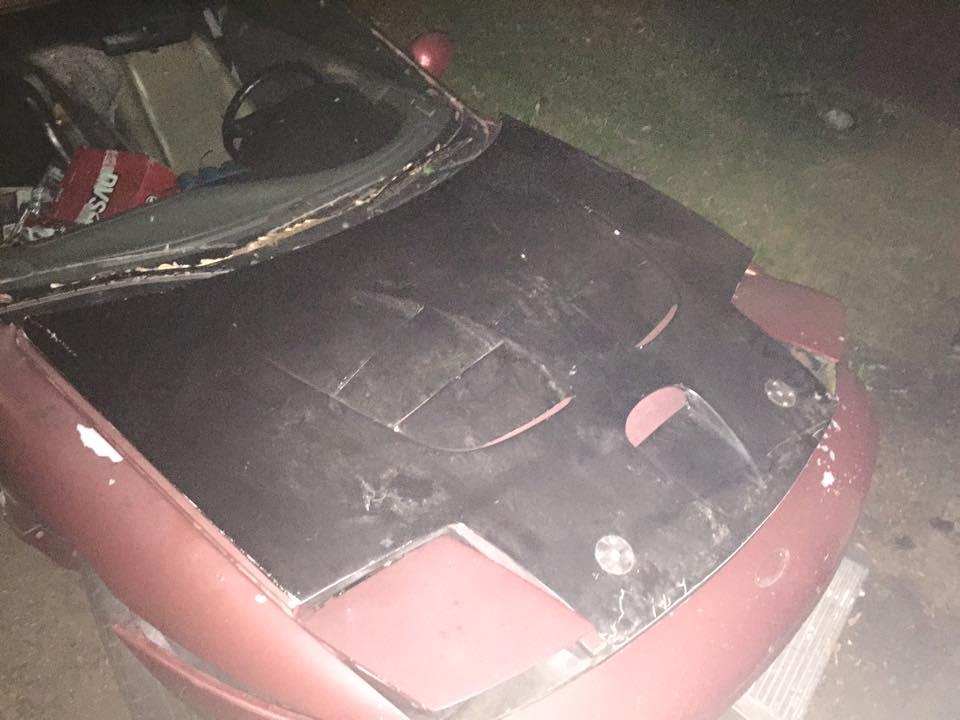 Red car with a modified black hood, front view.
