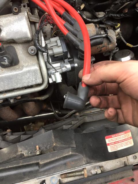 1995 Ford Probe - A mechanic's hand is shown holding a red spark plug wire near the engine of a car. A warning sticker with text in English and French is vis…