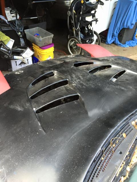 1995 Ford Probe - A close-up, slightly dusty view of a black car hood with prominent vents. The hood is positioned in a cluttered garage setting with a strol…
