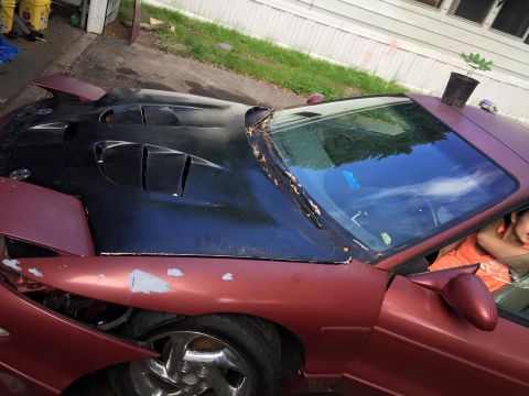 1995 Ford Probe - A close-up, high-angle shot of the front driver's side of a maroon car with a black hood featuring multiple vents. The car's paint is chipp…