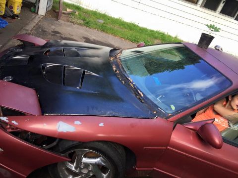 1995 Ford Probe - A close-up, high-angle shot of the front passenger side of a modified maroon vehicle. The custom black hood features multiple vents, and th…