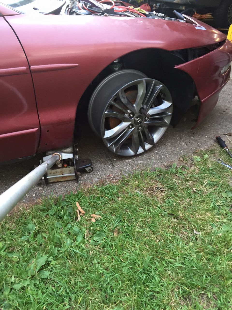Red car with front wheel removed, supported by a jack.