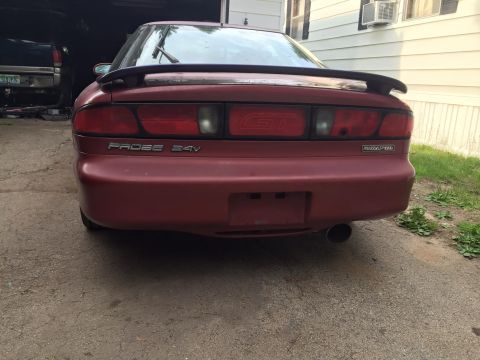 1995 Ford Probe - The rear view of a red 1995 Ford Probe GT with a spoiler and a visible exhaust pipe. The car is parked in a driveway with a house in the ba…