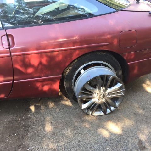 1995 Ford Probe - A red car with a flat tire and a spare wheel mounted on top of the flat tire. The spare wheel has a silver multi-spoke design and a red num…