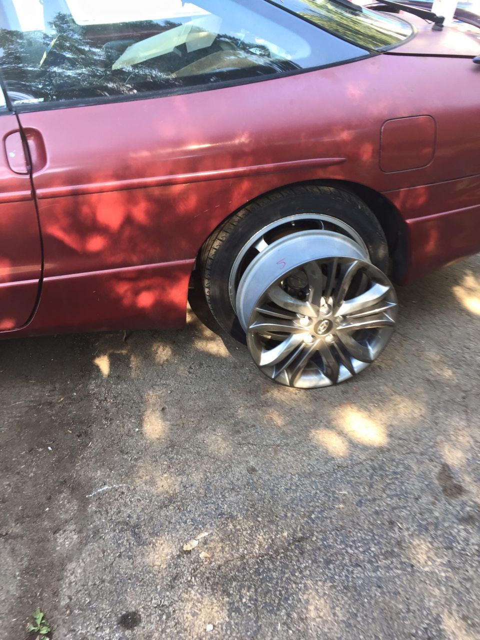 Red 1995 Ford Probe with flat tire and detached alloy wheel