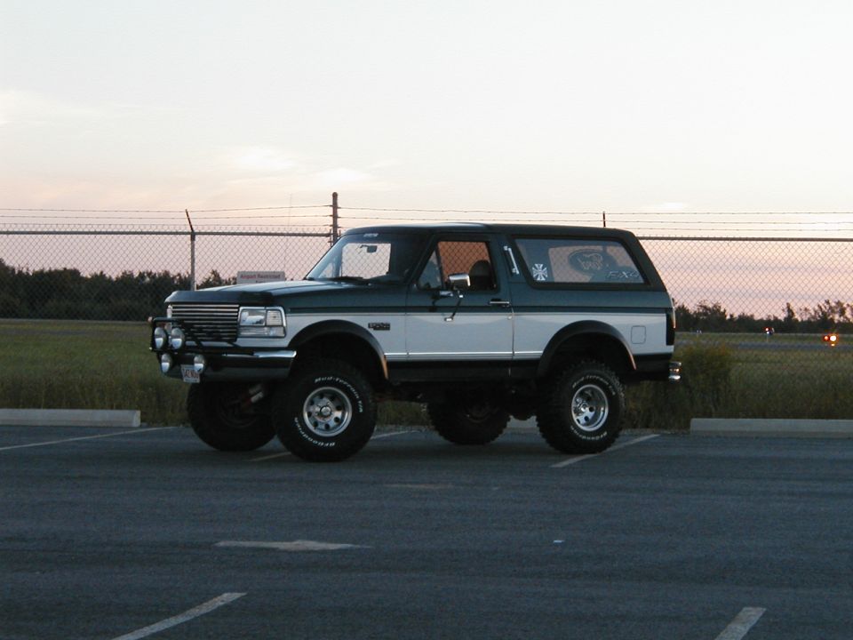 Lifted green and white full-size Bronco with hardtop and brush guard, side view at sunset