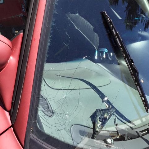 1995 Ford Probe - A close-up view of a cracked windshield on a red vehicle. A windshield wiper is visible on the right side of the frame.