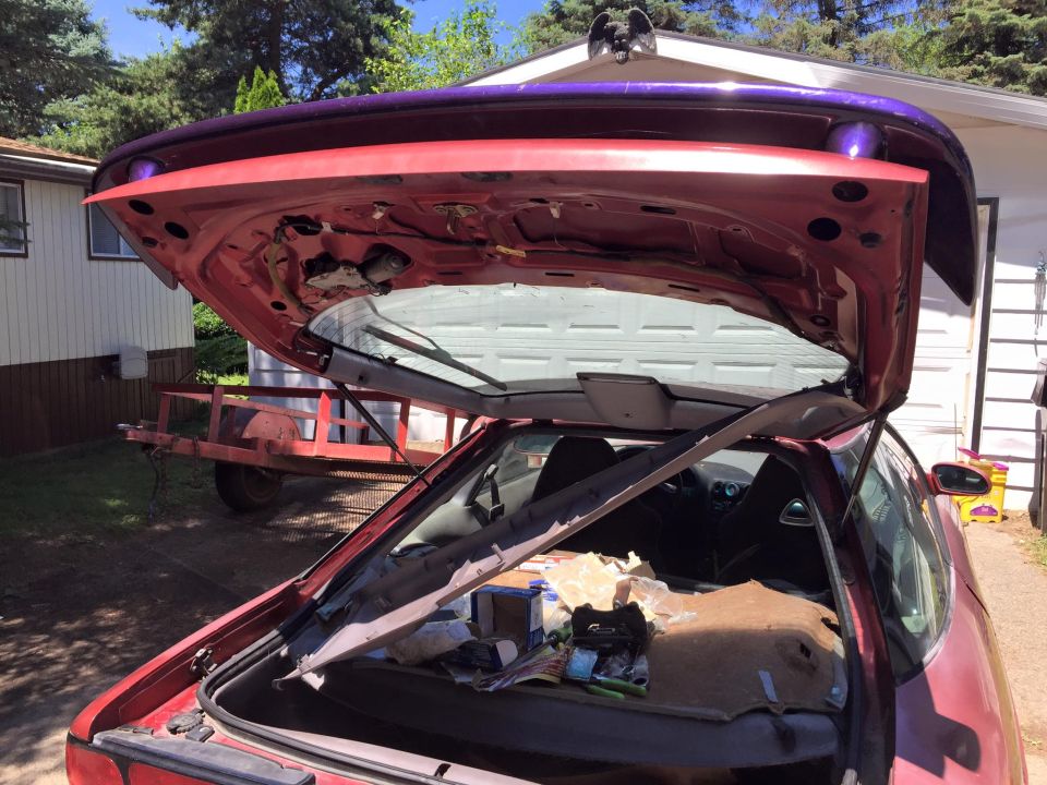 Red coupe with open trunk and hatch, showing interior and items in trunk. Trailer behind.