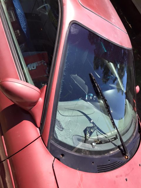 1995 Ford Probe - A close-up, overhead view of a cracked windshield on a red car. The car's hood and side mirror are visible, along with the interior dashboa…