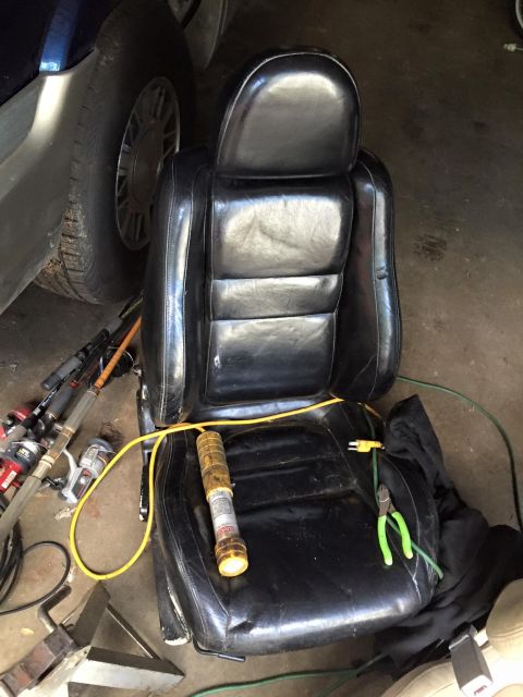 1995 Ford Probe - A black leather car seat is shown in a garage setting, with various tools and fishing rods nearby. A yellow cord runs across the seat, conn…