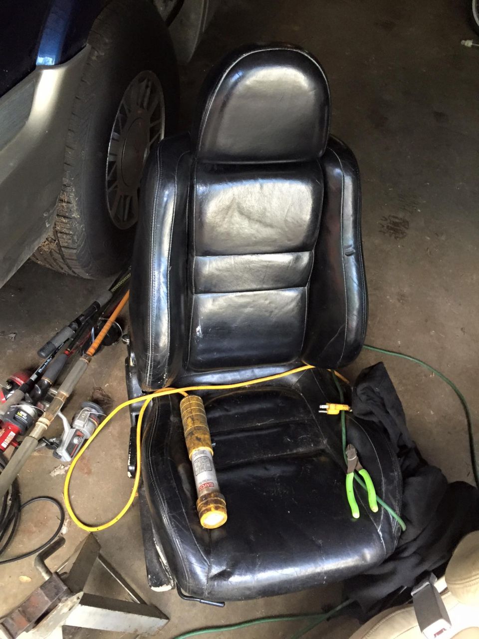 Black leather car seat with yellow cord, flashlight, and tools in a garage.