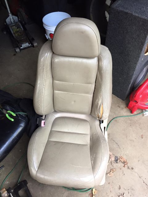 1995 Ford Probe - A tan leather car seat is shown in a garage setting, with visible wear and a tear on the right armrest. Various tools and equipment, includ…