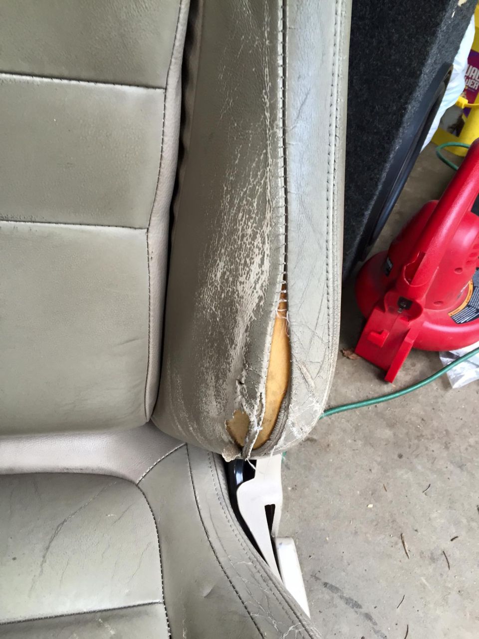 Damaged gray leather car seat with torn side bolster.
