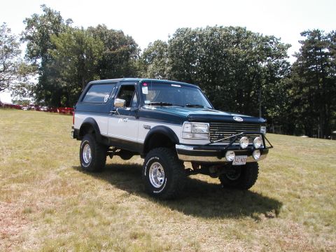 1994 Ford Bronco - This two-tone Ford Bronco is parked on a grassy incline under a clear sky.