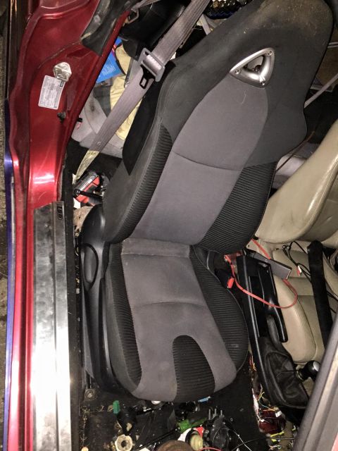 1995 Ford Probe - The interior of a red vehicle shows a racing-style driver's seat with a gray seatbelt. The floor and surrounding area are cluttered with ca…