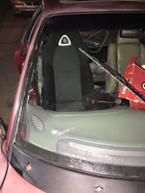 1995 Ford Probe - The interior of a red car is shown, focusing on the driver's seat and the damaged windshield. A racing seat with a triangular emblem is vis…