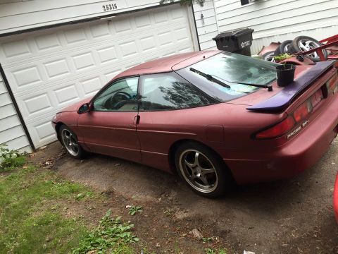 1995 Ford Probe - A maroon 1995 Ford Probe is parked in front of a white garage door. The car has a purple spoiler and aftermarket wheels.