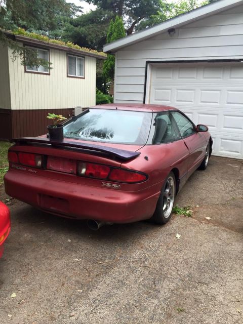 1995 Ford Probe - The rear passenger side of a red 1995 Ford Probe is parked in a driveway next to a white garage. A small potted plant sits on the rear spoi…