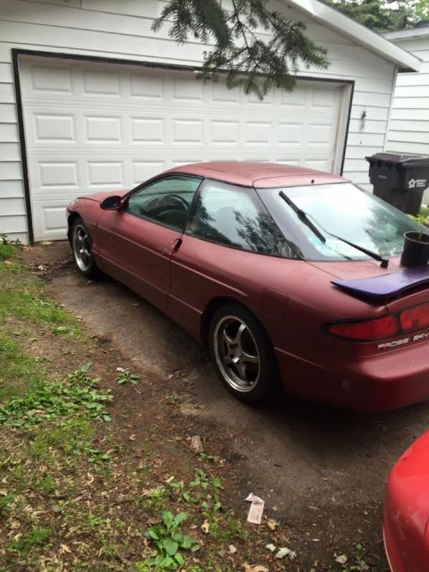 1995 Ford Probe - A maroon 1995 Ford Probe is parked in front of a white garage door. The car is viewed from the rear quarter angle, showing its coupe body s…