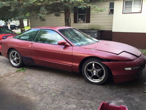 1995 Ford Probe - A dark red, two-door coupe is parked on a gravel driveway in front of a house. The car's hood is open, and the front bumper appears to be m…