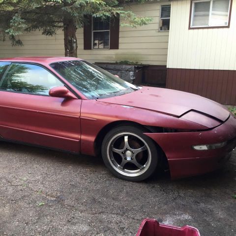 1995 Ford Probe - A red, two-door coupe sits parked on a gravel driveway in front of a house. The car's hood is slightly ajar, and the front passenger side f…