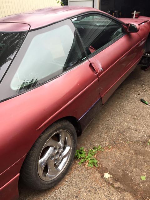 1995 Ford Probe - The right side of a dark red 1995 Ford Probe is shown parked on a gravel driveway, with the front wheel and part of the door visible. The c…