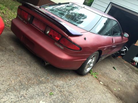 1995 Ford Probe - The rear driver's side quarter of a maroon 1995 Ford Probe is shown parked on a concrete driveway next to a garage. The car has a rear spoi…