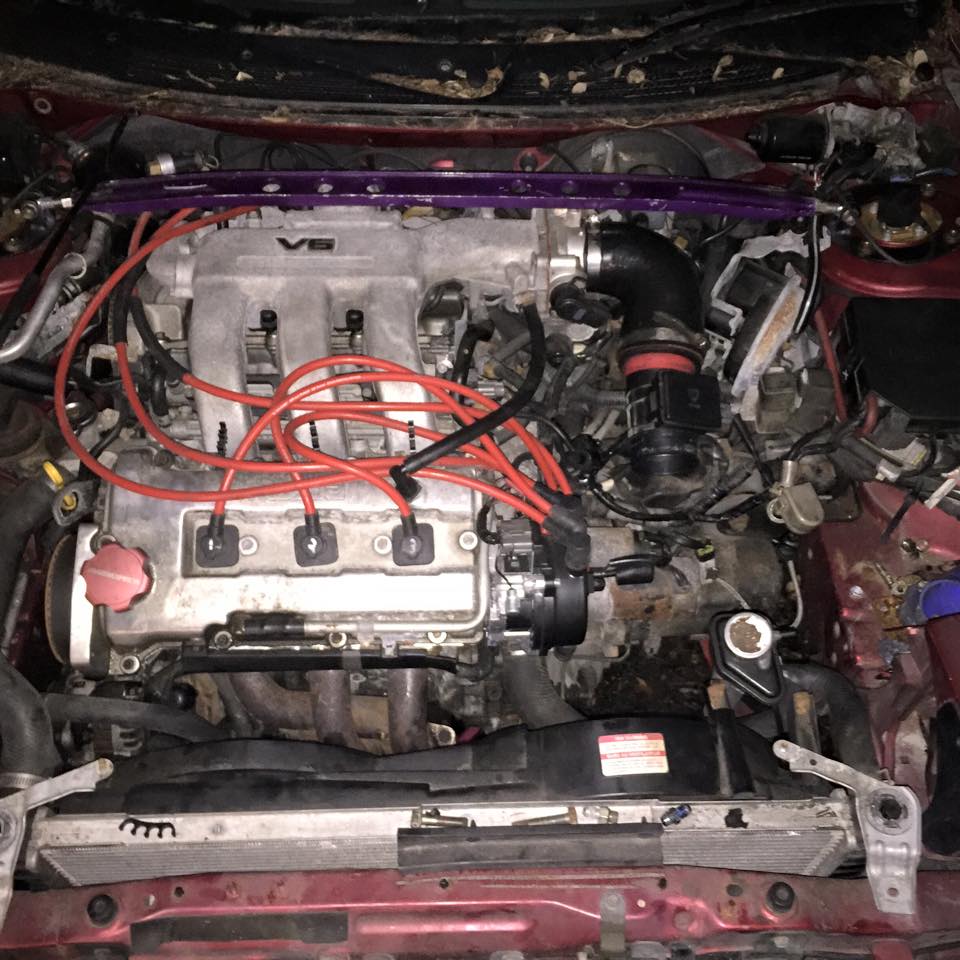 Red car V6 engine bay with purple strut bar and red spark plug wires.
