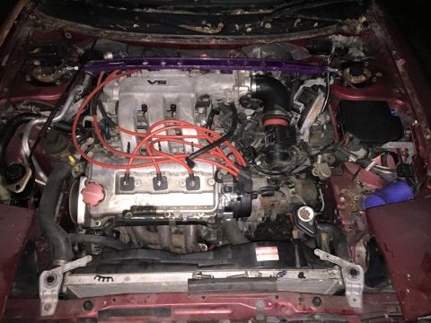 1995 Ford Probe - The engine bay of a red vehicle, likely a 1995 Ford Probe, is shown with a V6 engine, red spark plug wires, and a purple strut tower brace.…