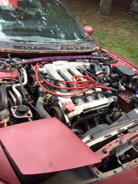 1995 Ford Probe - The engine bay of a red car is shown, with the hood partially open. The V6 engine is visible, along with red spark plug wires and a purple…
