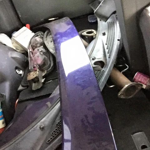1995 Ford Probe - A collection of car parts, including a purple fender or body panel and exhaust components, are stored in a vehicle's cargo area.