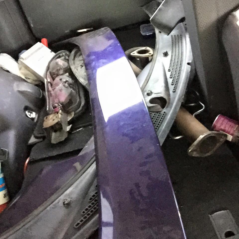 Purple car fender and exhaust parts in a vehicle's trunk.
