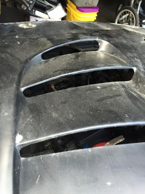 1995 Ford Probe - A close-up, dusty view of the hood of a dark-colored vehicle, showing three horizontal vents with chrome trim. Visible components and wirin…