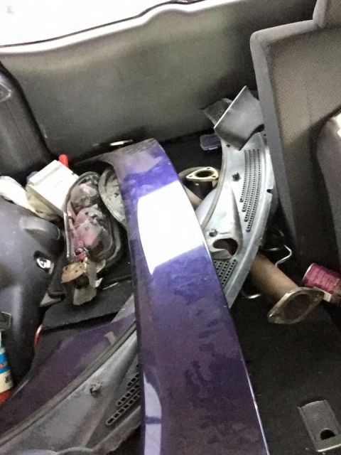 1995 Ford Probe - A collection of car parts, including a large purple body panel and exhaust components, are stored in the trunk of a vehicle.