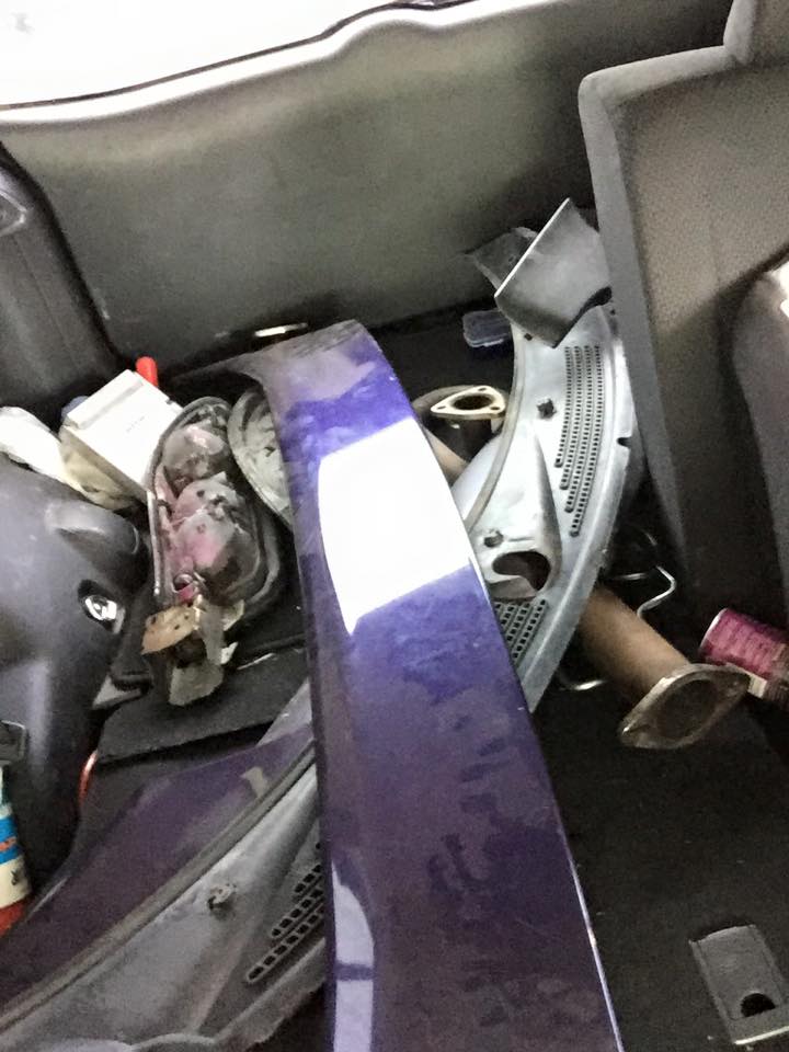 Purple car body panel and exhaust parts in a vehicle trunk.