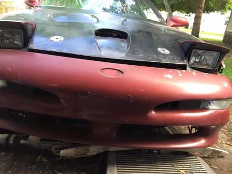 1995 Ford Probe - The front end of a dark colored car with a red bumper is shown. The car has pop-up headlights and appears to be undergoing some form of rep…