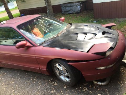 1995 Ford Probe - A maroon 1995 Ford Probe is parked outdoors on a paved surface with a person visible in the driver's seat. The car features a black afterma…