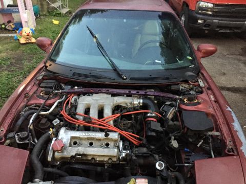 1995 Ford Probe - The engine bay of a maroon car is shown, with another vehicle visible in the background.