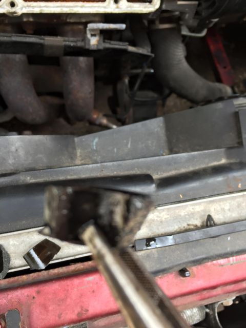 1995 Ford Probe - A mechanic's tool is positioned near the exhaust manifold and hoses within a vehicle's engine bay.