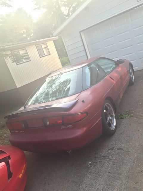 1995 Ford Probe - A red coupe is parked in front of a garage. Another red vehicle is partially visible on the left side of the frame.