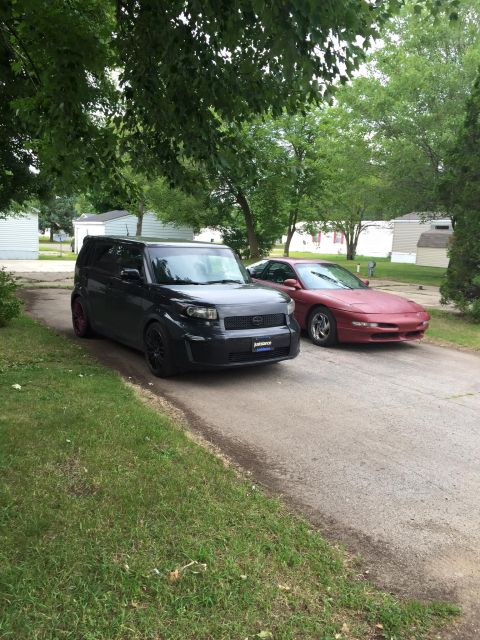 1995 Ford Probe - A red 1995 Ford Probe is parked on a driveway next to a black Scion xB.